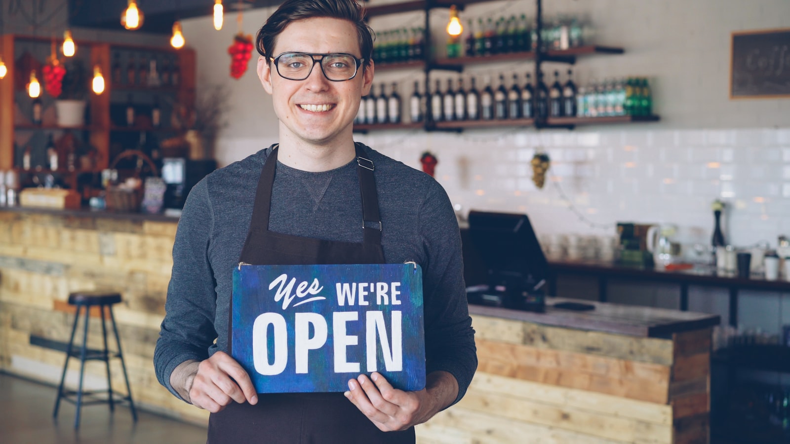 A confident business owner smiling and holding an open sign