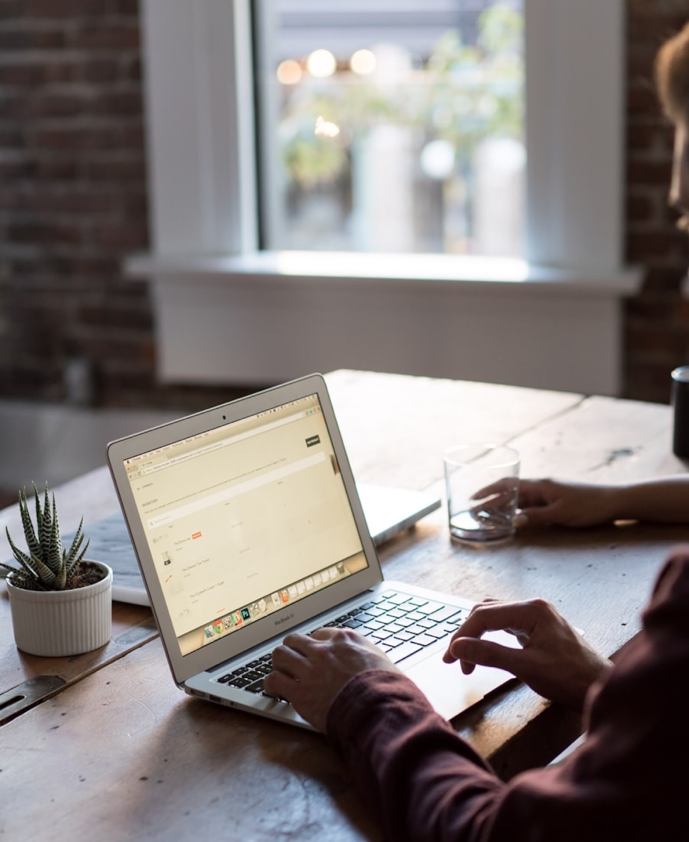 Hands typing on a laptop at a desk by a window